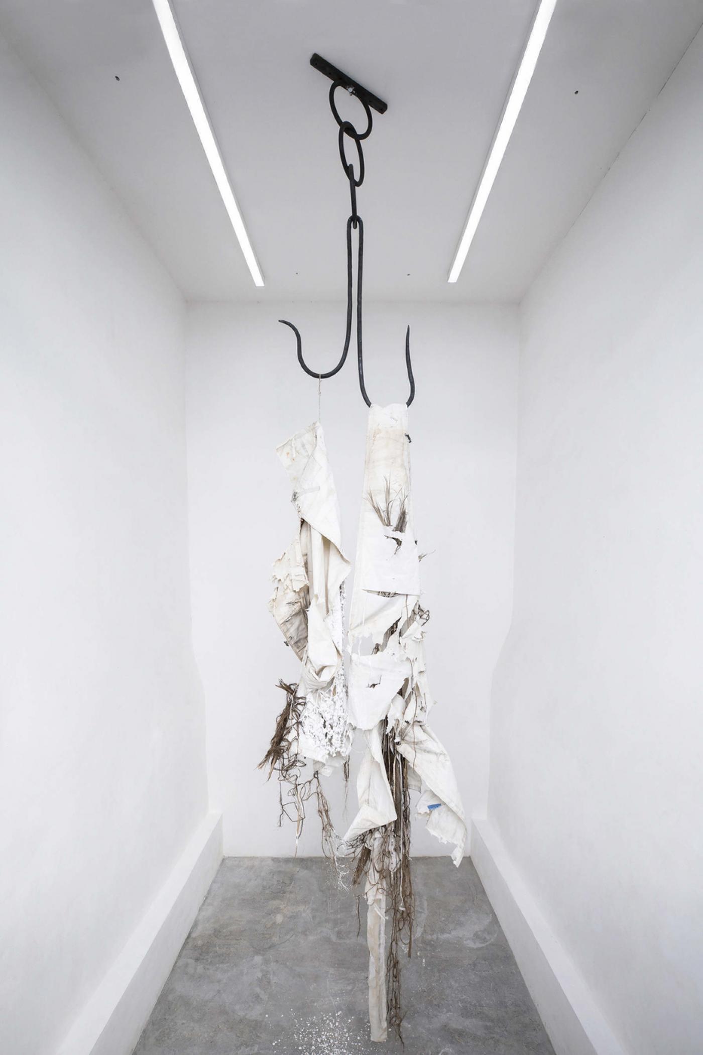 Dominique White, "Fugitive of the State(less)", 2019, voile détruite, feuilles de palmier, sisal goudronné, argile de kaolin, raphia, coquillages de cauris, crochet à viande à deux griffes, taquet, ancre, 680 x 160 x 110 cm.