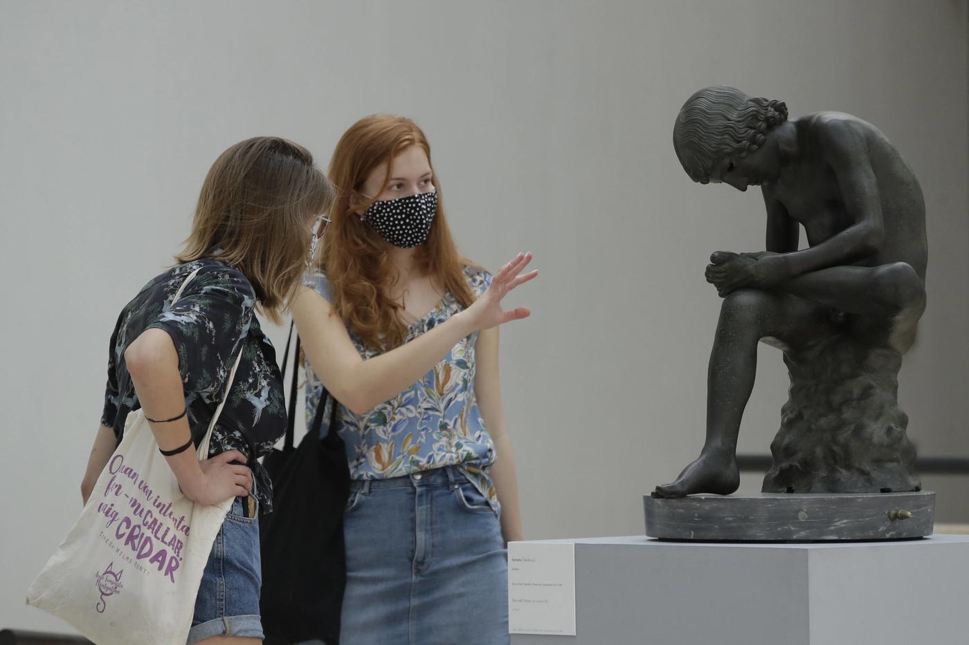 Des visiteuses masquées devant Le Tireur d'épine dans la salle des Triomphes du Palais des Conservateurs (Musées du Capitole) à Rome.