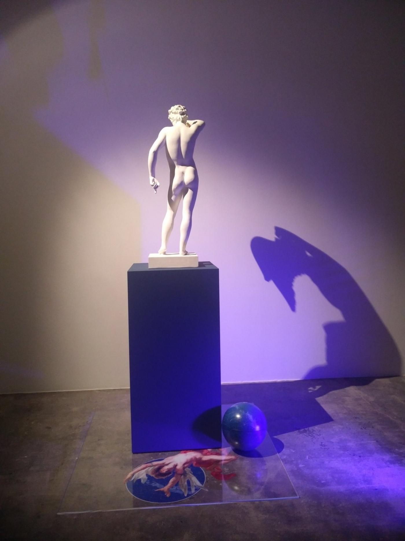 Giulio Paolini, In volo (Icaro e Ganimede), 2019, statue en plâtre, deux ailes dorées en papier cartonné, socle bleu, plâque en Plexiglas, globe, cartes célestes, fragments de reproductions photographiques, lampe de Wood, 241 x 245 x 190 cm.