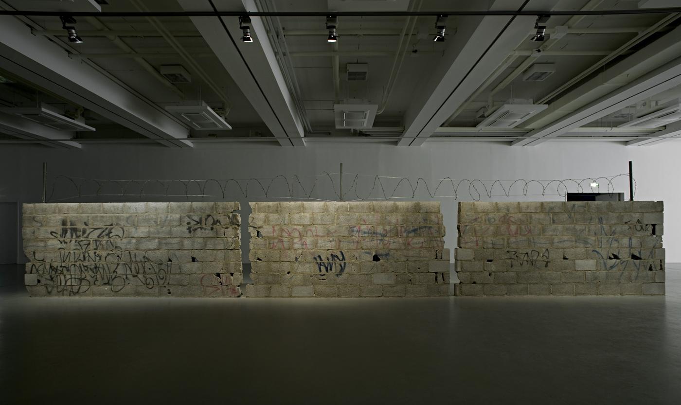 Teresa Margolles, Muro Ciudad Juárez, 2010, blocs de béton, fils de fer barbelés et trous d'armes résultant d'une fusillade liée au crime organisé à Ciudad Juarez, au Mexique.
Coll. Frac Grand Large, Hauts-de-France, Dunkerque. Vue de l'installation à l'exposition "Teresa Margolles: Frontera, Fridericianum", Kassel, Allemagne, 2010.